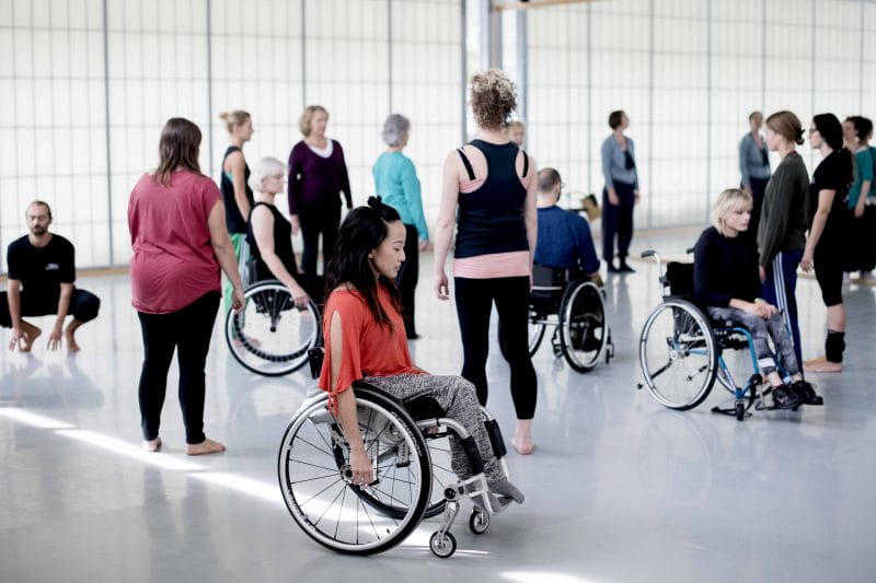 Youth Dance Class. Dancer using wheelchair looks to be moving across the space with other dancers in the background