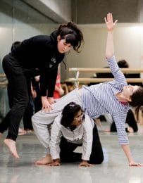 3 dancers move together, one knees with another leaning back over them and another jumps to the side