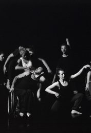 Black and white image of group of disabled and non-disabled dancers moving as a group facing camera