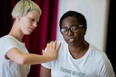 Two dancers, one eyes closed leaning forward. the other pushing their right hand against the front of the other's right shoulder