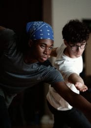 Two dancers leaning forward, arms reaching toward camera