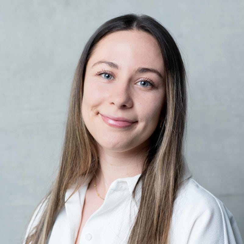 Louisa Sutherland has long, straight, light brown hair. She is smiling and wearing a white shirt