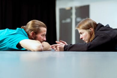 View from studio floor, two dancers lying down, face each other in conversation