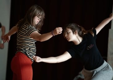 Two people dancing in front of one another with their arms stretched sideways.