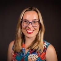 A headshot of a smiling woman with long blonde hair and blue framed glasses